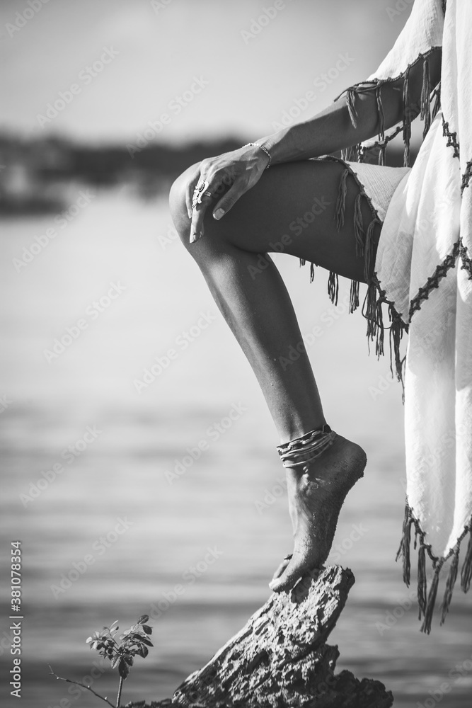 Wall mural woman leg and hand lean on tree on beach boho vibes look in white  tassel dress black and white - Wall murals