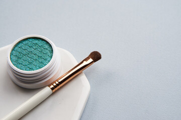 Green eyeshadow and makeup brush on white stand isolated background