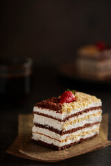 Piece of cake honey cake decorated with strawberries, on a dark background