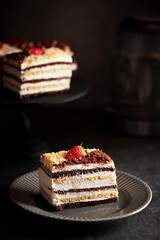 Piece of cake honey cake decorated with strawberries, on a dark background
