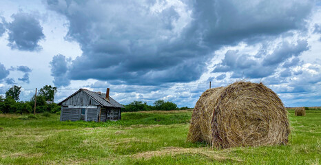 Rural landscape with harvesting field, hayroll and small old house
