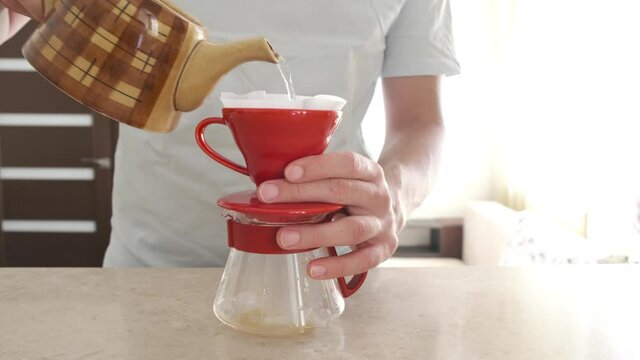 Homemade coffee. Pourover. A man brews at home v 60. He pours hot water into a red ceramic dripper with a filter and coffee drips into a glass server