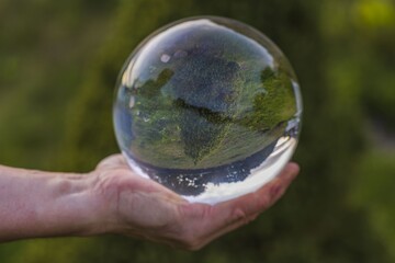 Close up macro view of hand holding crystal ball with inverted image of green natural landscape