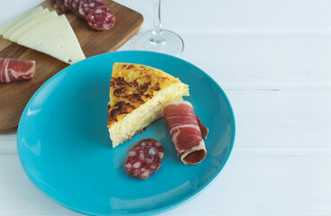 Piece of Spanish omelette on a blue plate with ham on a white background. Typical food concept. Copy space.