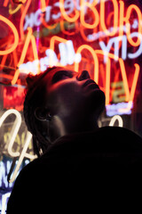 A hooligan girl stands against the background of a neon sign in the evening in the city.