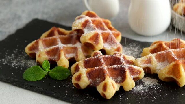 Slow motion confectioner sugar decorating belgian waffles. Pastry chef serving sweet dessert waffles