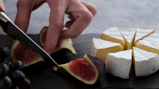 Cutting figs and camembert cheese. Preparing cheese platter with french cheese and fruits