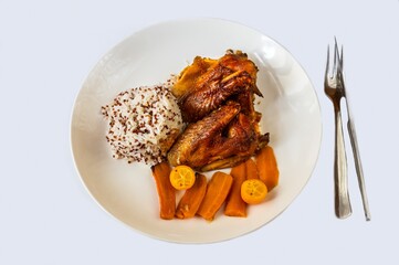 Baked hen with carot and kumquat, rice with quinoa on white plate on white backround.