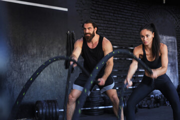 Fototapeta na wymiar Athletic young couple with battle rope doing exercise in functional training fitness gym.