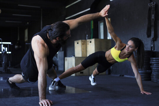 Sporty couple doing push ups and giving high five to each other in gym.