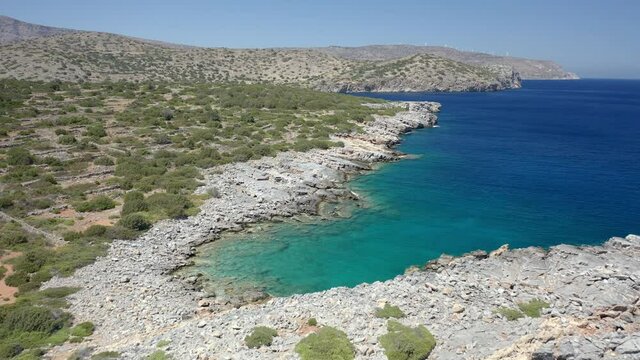 Aerial drone flying low over a dry, rocky coastline and crystal clear ocean (Crete, Greece)