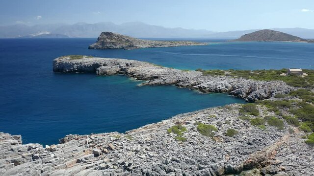 Aerial drone flying low over a dry, rocky coastline and crystal clear ocean (Crete, Greece)