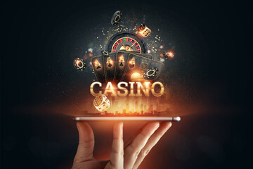 In a man's hand a smartphone with playing cards roulette and chips, black-gold background. Concept of online gambling, online casino. Copy space
