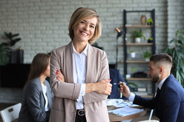 Business woman with her staff, people group in background at modern bright office indoors.