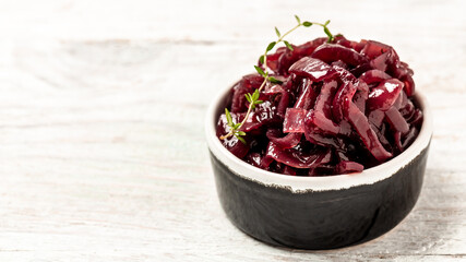 Red onion chutney in ceramic bowl isolated on white wooden table. Vegetable jam. Delicious sauce. Gourmet