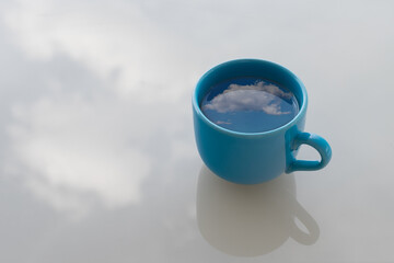 The sky and clouds are reflected in a cup of coffee or tea.