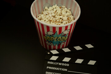 Striped popcorn box movie clapper on black background. 
Tasty salty popcorn. 