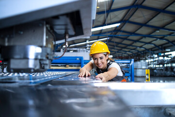 Female factory worker in protective uniform and hardhat operating industrial machine at production line. People working in industry.
