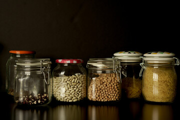 Legumes, lentils, chickpeas and beans assorted in different jars on a black background. Front view.