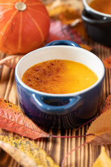 orange Creme Brulee aus Kürbis vom Hokkaido mit  karamellisierter Zuckerkruste in Förmchen auf einem braunen Holztisch mit Laubblättern im Herbst
