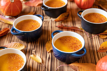 orange Creme Brulee aus Kürbis vom Hokkaido mit  karamellisierter Zuckerkruste in Förmchen auf einem braunen Holztisch mit Laubblättern im Herbst