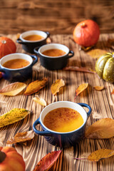orange Creme Brulee aus Kürbis vom Hokkaido mit  karamellisierter Zuckerkruste in Förmchen auf einem braunen Holztisch mit Laubblättern im Herbst