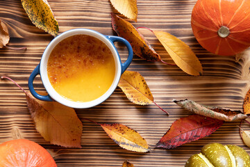 orange Creme Brulee aus Kürbis vom Hokkaido mit  karamellisierter Zuckerkruste in Förmchen auf einem braunen Holztisch mit Laubblättern im Herbst