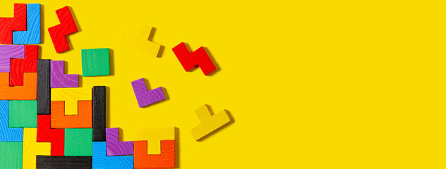 Different colorful shapes wooden puzzle blocks on yellow background. Geometric shapes in different...