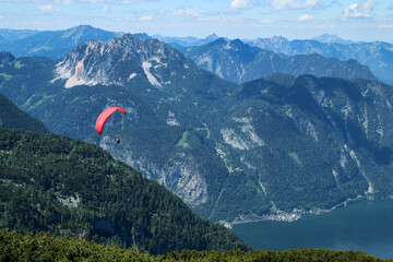 The paraglides are flying above the mountains high in the blue sky and enjoying the view. 