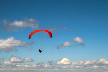 The paraglides are flying above the mountains high in the blue sky and enjoying the view. 