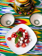  caprese salad with mazzarella tomatoes and herbs in oriental style on a table with a teapot and a cup for tea.