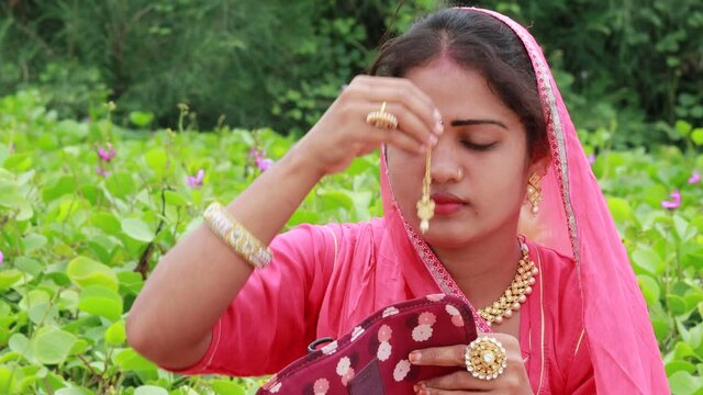 An Indian beautiful woman smiling while sitting in the garden wearing a Rakhdi  (Marwari brides call it as maang tikka) . A gorgeous Adult female model Traditionally wore pink colored headscarf 