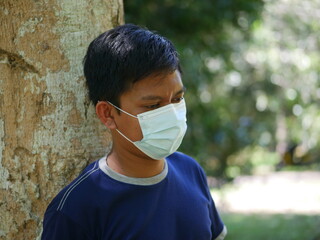 Handsome Indonesian young man wearing face mask, standing in the park. Portrait of confident Indonesian young man wearing face mask at park during coronavirus