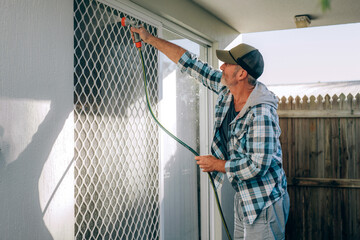 Caucasian adult middle aged bearded man cleans window and sliding door with flow of water by hose pipe
