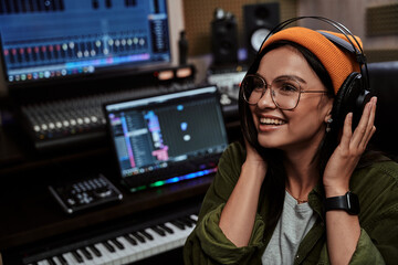 Close up portrait of beautiful young brunette, female artist smiling aside, adjusting headphones...