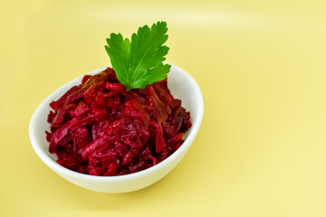 Grated beets. Fresh beet salad in white bowl isolated on yellow background. Healthy food concept, diet, fresh vegetables, vitamins and liver recovery.