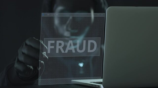 Hacker wearing black mask pulls FRAUD tab from a laptop