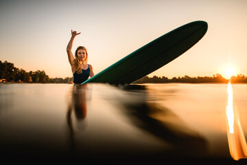 pretty woman sitting on surf style wakeboard on water and showing hand gesture