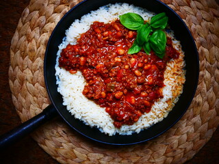 Chili con carne with rice and fresh basil in a cast iron skillet