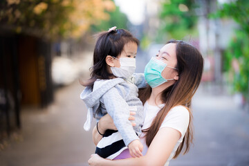 Family carried child. Mother and daughter wear medical face mask. Mom smiled at little girl. Concept of prevention of the spread of coronavirus disease (Covid-19) and small toxic dust pm 2.5.