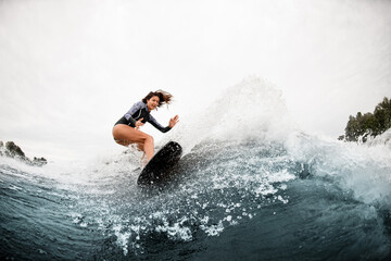 View of woman in swimsuit who engaged in extreme sport and rides board on river wave