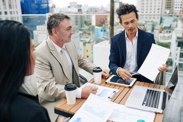 Serious mixed-race financial analyst showing report to colleagues at meeting