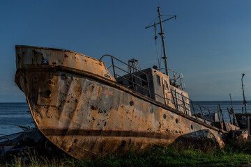 old rusty fishing boat, vessel on grassy shore, coast of lake Baikal, blue sea in light of sunset