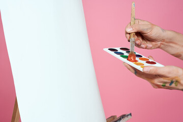 artist with paints and brush in hands easel drawing art hobby pink background