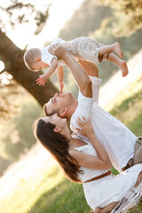 mom, dad lifts high his baby boy up mid air and looks at her smiling. Happy parents spending time playing with son in park on summer day. selective focus