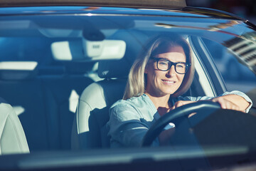 Happy attractive caucasian woman wearing eyeglasses driving her modern car through the city on...