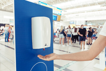 A female passenger disinfects her hands with an automatic sanitizer dispenser in the airport....