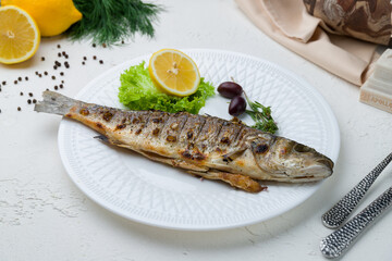 Fried sea bass on the grill, on white plate with lemon