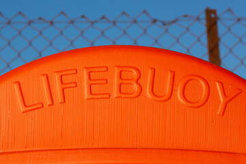 The word lifebuoy on an orange container that hold a life ring