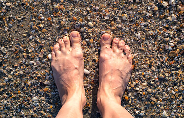 Female feet on the sea sand from seashells, top view. Natural look. Vacation and travel concept.